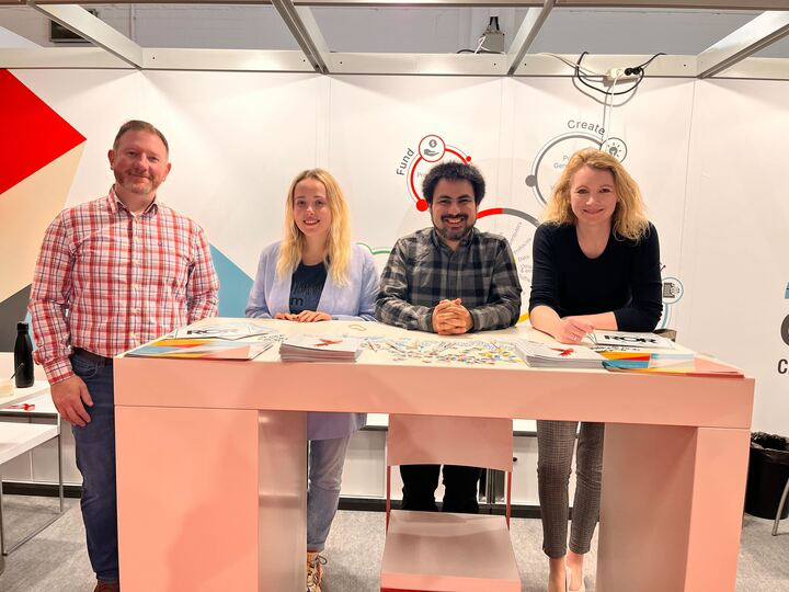 photo of Paul, Maryna, Luis, and Helena at the table at the booth
